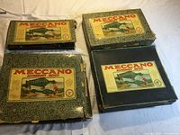 Four Meccano accessory outfit boxes labeled 1, 2, 3, and 4, all worn with vintage artwork on lids