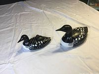 Photo of two black and white painted pottery loons placed on a white cloth. One is a larger single bird, the other is a smaller mother loon with a baby on her back.