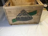 Front side of wooden crate showing Pure Spring logo with crown and green stripe accents, some paint chipping and wear visible