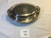 Silver plate oval serving dish with lid closed, showing decorative beaded edges and ornate side handles on lid.
