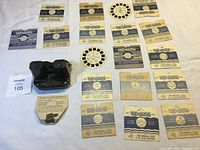 Full lot overview with Sawyer View-Master Model C viewer in black with 18 View-Master slide reels in paper sleeves spread around it, plus instructional insert.