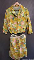 Photo of 1960s floral jacket and skirt hanging together, showing full length and front details.