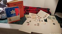 Various international postage stamps mounted on white sheets and in small booklets alongside a red plaid cloth background.