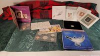Coin and stamps displayed on fabric, including stamps sheets, coins in plastic holders, booklet, and packaging.