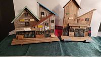 Wide view of two driftwood fishing village decorative houses with varying roof colors and dock bases on green cloth surface.
