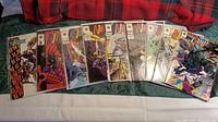 Nine Ninjak comic books issues #1-9 laid out side-by-side in protective sleeves on green tablecloth with red plaid fabric background