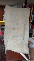 Full view of the cream-colored lamb wool cover hanging vertically, showcasing its fluffy texture and size.