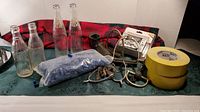 Wide shot showing all items including four soda bottles, blue tubing, fishing gear, tape rolls, and plaid cloth