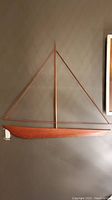 Side view of teak sailboat wall art mounted on wall showing hull, mast, and sails outline.