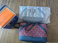Photo showing one blue soft cooler box with an orange lid, one large red diamond patterned insulated bag, and a second large chiller bag in pastel stripe colors still in packaging.