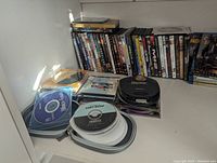 Shelf showing DVDs lined up with spindles of discs front left and a CD player on top