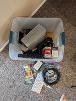 Top view of plastic box filled with electronic items such as power supply, remotes, cables, and accessories along with items outside the box including keyboard, cables and packaged USB and batteries.