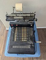 Front view of a large vintage mechanical adding machine showing the keyboard with many round keys and the paper roll on top.