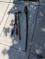 Photo of three large hand tools laid on a concrete surface including a sledgehammer, lopper, and ratchet pipe wrench