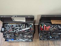 Two dark metal toolboxes with open lids and multiple drawers filled with assorted machining tools