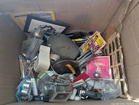 Top view inside of cardboard box showing various small miscellaneous items including pouch, pens, cord box, keys, and metal tools.