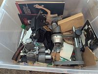 Overview of items including binoculars, gloves, camera accessory, and book inside plastic tote.
