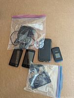 Four mobile phones and chargers on cardboard surface in plastic bags, showing devices with black cases, flip phone, and accessories.