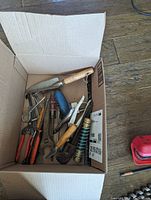 Box with assorted metal hand tools such as pliers, a wrench, putty knife with wooden handle, scissors and tape measure