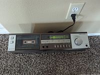 Front angled photo of Realistic SCT-500A cassette tape deck plugged in and powered on, cassette inside, LED level meters lit up.