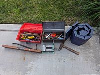 Full view of lot showing two metal toolboxes, roll-up padded tool container, wooden mallet hammer, crowbar, and bench vise alongside