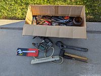 Box open showing assorted tools inside, including electric drill, wrench, hammer, and power strip.