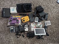 Photo showing entire assortment of various untested electronic devices including radios, cameras, GPS, and accessories arranged on carpet.
