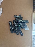 Top view of 13 various remote controls piled on a couch surface.