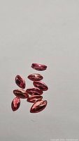 Close-up of a group of orange-pink marquise-shaped padparadcha sapphires on white background.