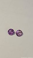 Two round cut amethyst gemstones placed side by side showing color and cut.