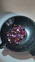 Parcel of small round cabochon rhodolite garnet gemstones in a black container, colors purple, red, pink.