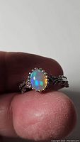 Close-up view of the oval Ethiopian opal with a multicolored flash set in a silver ring held by fingers.