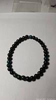 Full view of dark green, opaque emerald bead bracelet laid flat showing round beads on elastic cord.