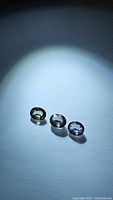Three small oval faceted untreated Tanzanian sapphires displayed on a white surface under bright light to show clarity and color variations.