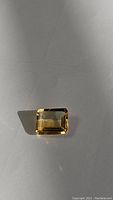 Golden citrine gemstone on a light surface, showing emerald cut and golden yellow hues.