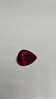 Close-up image of a pear-shaped red ruby gemstone on a white background showing its vivid red color and faceted cut.
