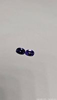 Two deep purple blue oval cut tanzanite gemstones laying side by side showing color and clarity.