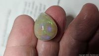 Pear-shaped opal cabochon held between thumb and forefinger showing play-of-color