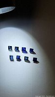 Eight small square cut natural royal blue sapphires arranged together under direct light showing deep blue color and clarity.