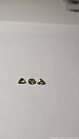 Three natural chartreuse sapphires on white background showing two trillion cut and one oval cut stones.