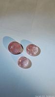 Three natural strawberry quartz round cabochons placed on a white surface with light and shadow showing translucency and inclusions