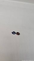 Two oval cut gemstones on white background, blue-purple tanzanite at left, red-orange sapphire at right