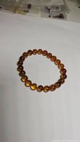 Photo of one amber bead bracelet with round polished beads on elastic cord, warm amber color, smooth finish, slight variations in bead shade.