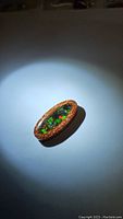 Oval dinosaur bone pendant with central amolite inlay under clear epoxy, showing vibrant multi-color flash, on neutral background illuminated with direct light.