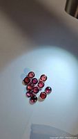 13 round cabochon cut stones on white surface under directed light showing purple-pink color and transparency.