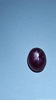 Natural red star ruby oval cabochon gemstone on a light surface showing the star pattern