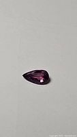 Pear-shaped purple sapphire gemstone on plain background, showing color and cut detail, untreated no heat natural stone.