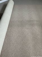 Partial view of beige rug showing the subtle texture and pattern on its surface and the rolled edge.
