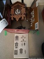 Cuckoo clock inside a cardboard box with instruction manual sheet visible.