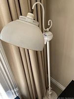 Side view of the metal floor lamp showing curved arm and metal shade near beige curtains.